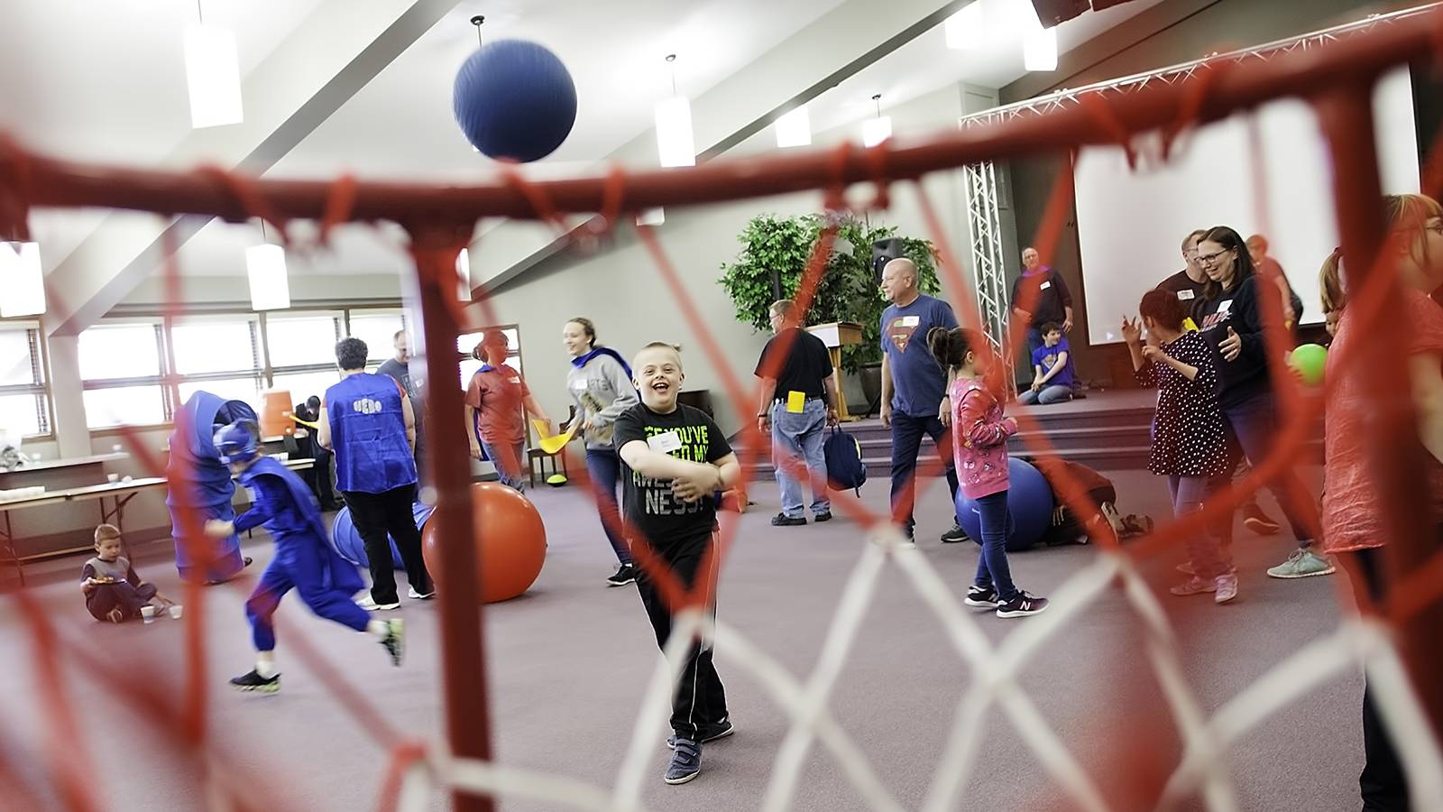 A boy throws a ball through a basketball hoop. Viewed through net.