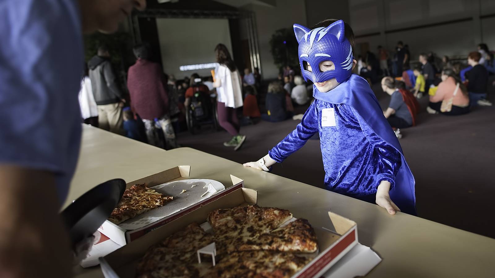 A child in a superhero costume selects pizza